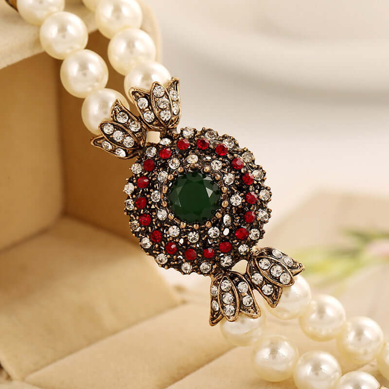 Luxury pearl bracelet with an intricate green and red gemstone clasp, showcased on a soft velvet box.